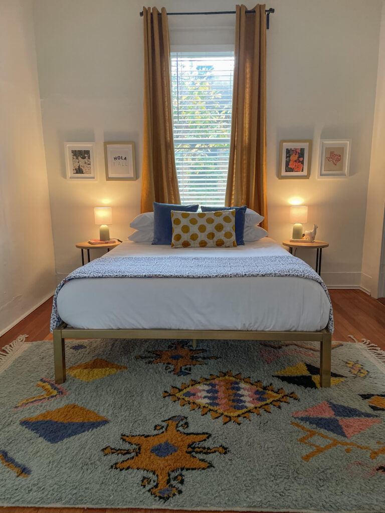 A vibrant Airbnb living room with local artwork and a city-themed coffee table book. Simple white linens with a few accent pillows and a throw are a perfect way to style your beds in your airbnb. 
