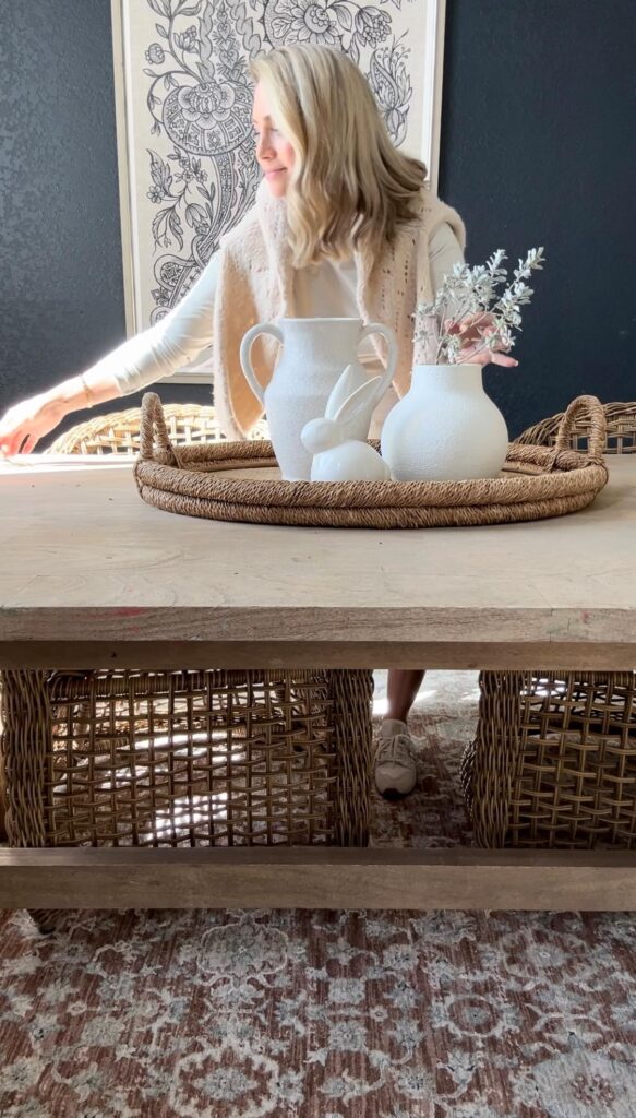 Styled Easter centerpiece with a rattan tray, faux flowers, a bunny, and ceramic eggs on a dining table.
