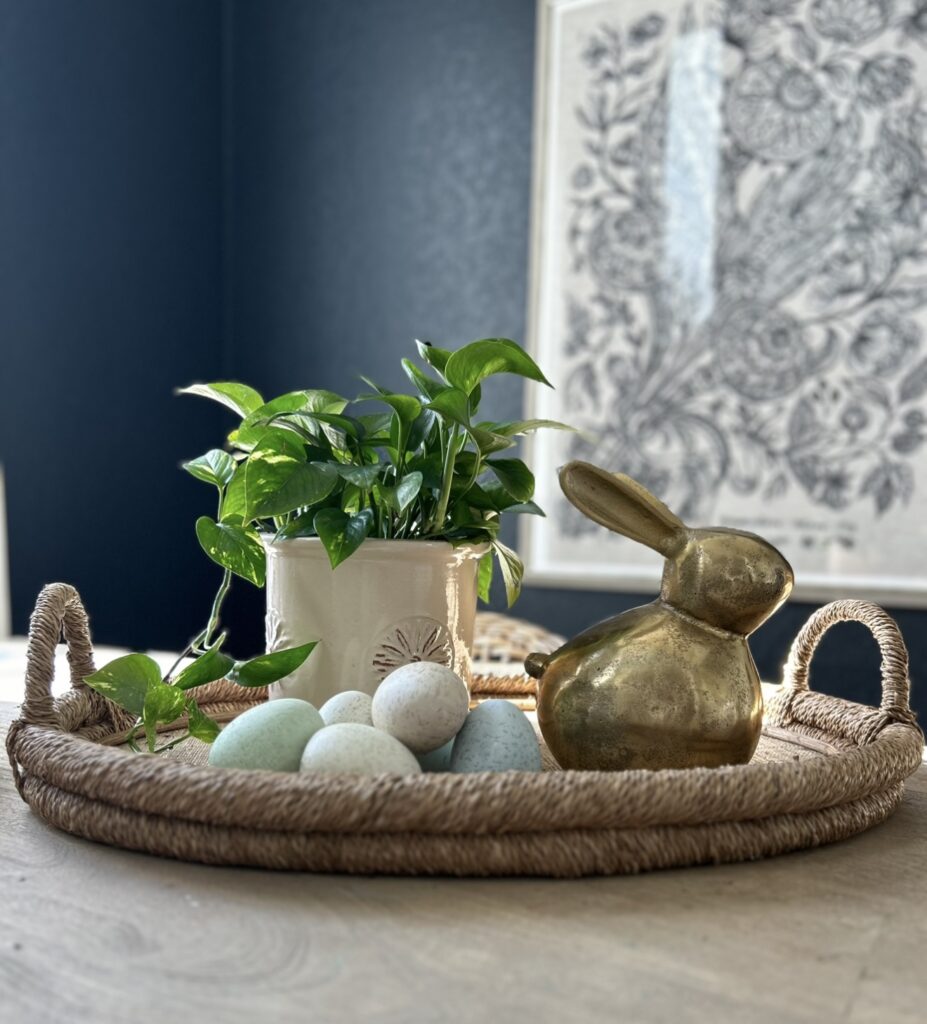 Single image featuring a plant in a decorative pot alongside a wooden bunny and ceramic eggs for a stylish Easter display.