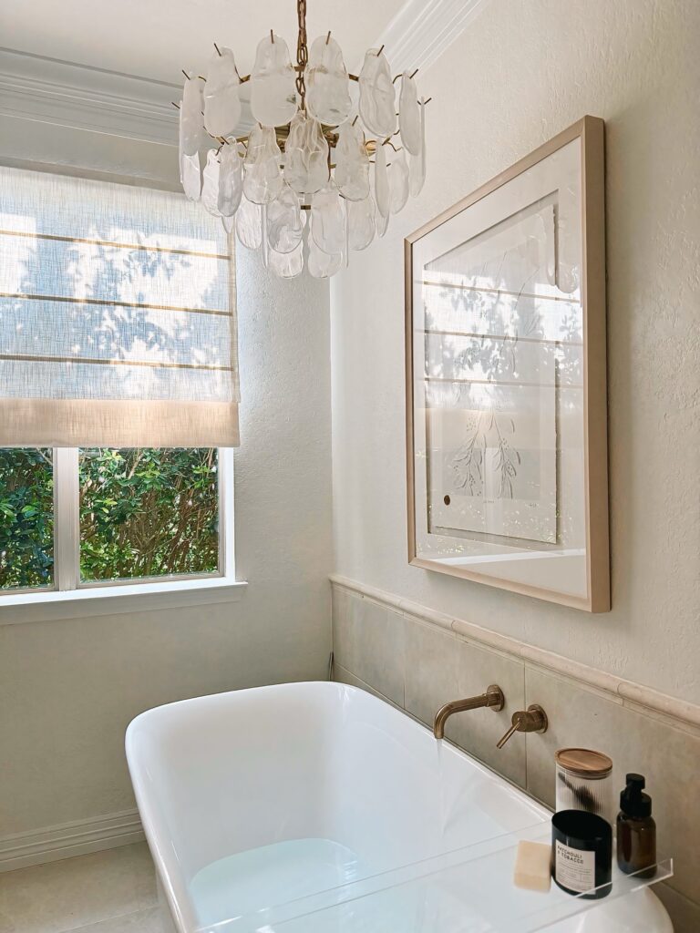 Renovated bathroom featuring a luxurious new bathtub, elegant chandelier, and a stylish Two Pages Roman shade for a spa-like ambiance.